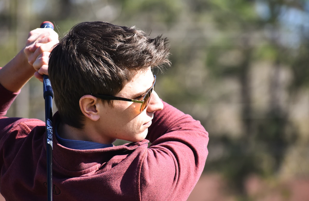 A young golfer wearing PeakVision sunglasses at the top of his swing